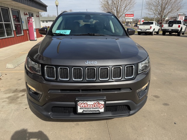 Front view of a dark gray Jeep SUV at a car dealership, with a sale tag on the windshield.