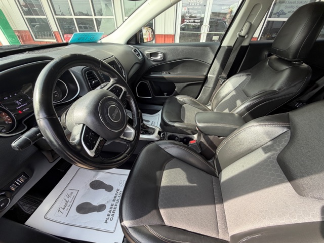 Interior of a car showing the steering wheel, dashboard, and two front seats with black upholstery.