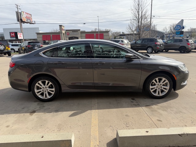 Side view of a gray four-door sedan parked in a parking lot with other cars and storefronts in the background.