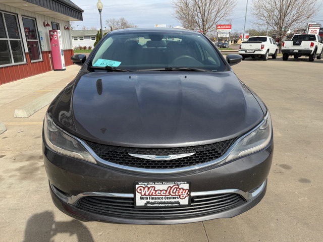 Front view of a dark gray Chrysler sedan at a car dealership, teal price tag on the windshield, Wheel City Auto Finance Centers license plate frame, other cars in the background.