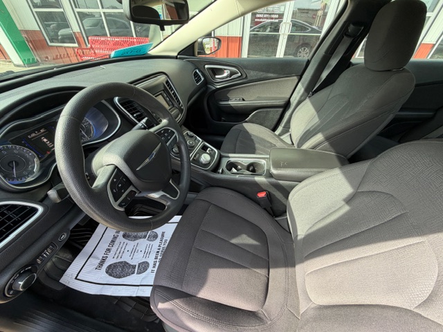 Front interior of a car showing steering wheel, dashboard, center console, and two front seats; paper floor mat on the driver’s side.