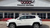 White Jeep Compass SUV parked in front of Wheel City Auto Finance Centers storefront with large windows and red accents.