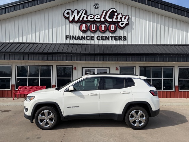 White Jeep Compass SUV parked in front of Wheel City Auto Finance Centers storefront with large windows and red accents.