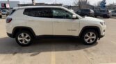 Side view of a white Jeep Grand Cherokee SUV parked in a dealership lot, with other cars in the background.