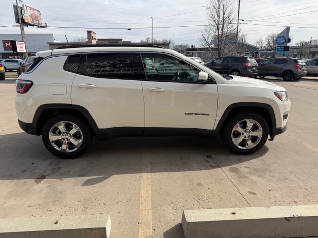 Side view of a white Jeep Grand Cherokee SUV parked in a dealership lot, with other cars in the background.