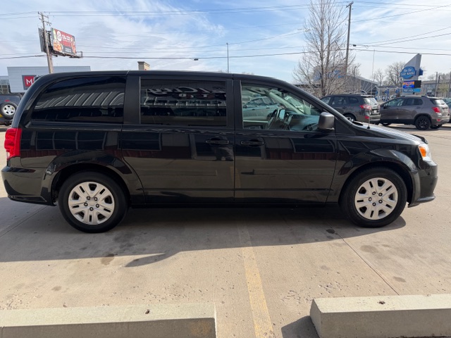 Side view of a black minivan parked in a sunny parking lot with tinted windows and silver wheels, nearby cars in the background.