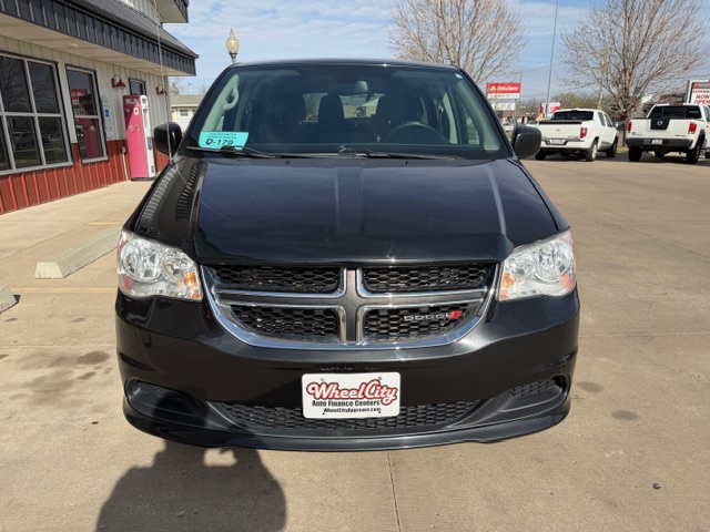 Front view of a black Dodge minivan at a car dealership, chrome grille and Wheel City plate visible.
