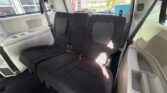 Interior of a minivan with a black fabric three-row bench seat, visible seat belts, and cup holders along the left side.