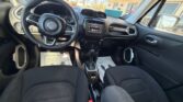 View of the car’s front interior: black fabric seats, a steering wheel with a Jeep logo, a center touchscreen, gear shifter, and a dashboard with air vents; driver and passenger areas visible from the front cabin with the outside scene through the windows.
