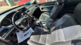 Interior view of a black leather Honda sedan with the driver’s seat and front passenger seat, steering wheel, dashboard, and center console visible from the open driver's door. Outside shows a building.