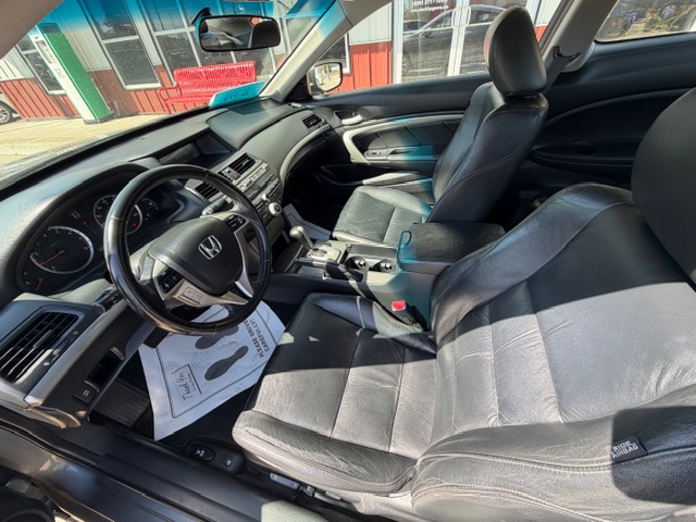 Interior view of a black leather Honda sedan with the driver’s seat and front passenger seat, steering wheel, dashboard, and center console visible from the open driver's door. Outside shows a building.