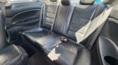 Back seat of a car with black leather upholstery, three seating positions and headrests, sunlit interior from the side window.