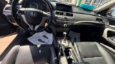 Interior view of a black Honda sedan from the driver's side, showing the steering wheel, center console, and front seats with dealer papers on the floor.