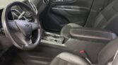 Driver's seat area of a dark interior sedan, steering wheel and center console visible, red-stitched black leather seats