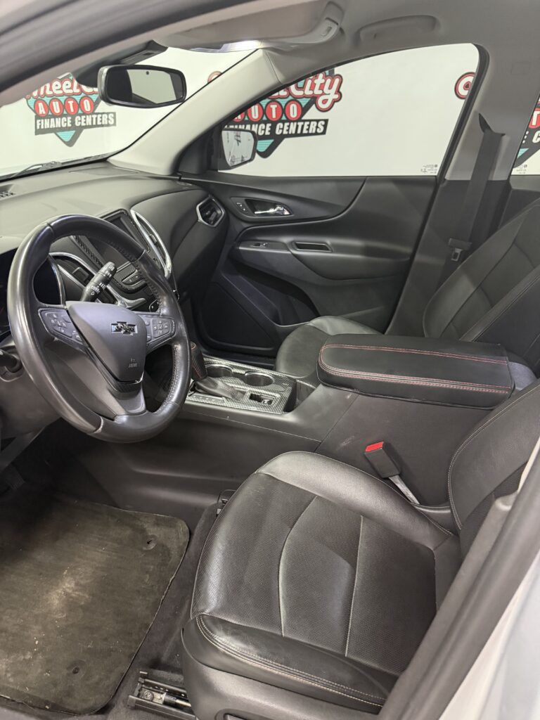 Driver's seat area of a dark interior sedan, steering wheel and center console visible, red-stitched black leather seats