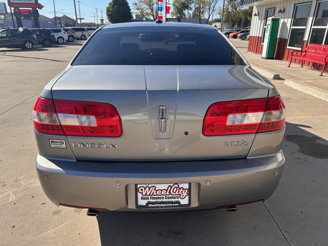Rear view of a silver Lincoln MKZ parked at a dealership lot; visible Lincoln emblem, MKZ badge, and Wheel City Auto Finance Centers license plate frame, red taillights prominent.