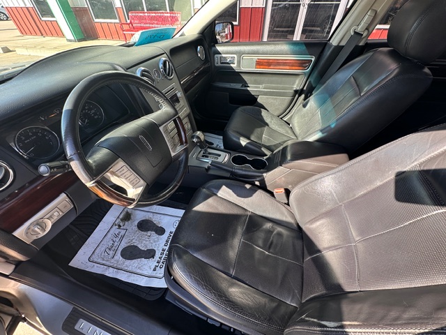 Front interior of a car with black leather seats, steering wheel, center console, and cup holders visible in daylight.