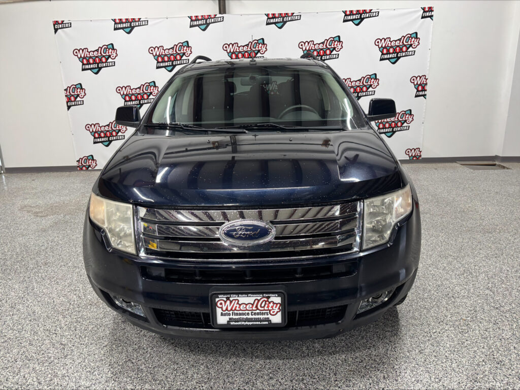 Front view of a dark blue Ford SUV inside a showroom with a white backdrop branded 'Wheel City Auto Finance Centers' repeated across the wall.
