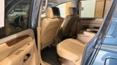Blue SUV interior with beige leather seats; open rear door showing captain chairs and front seats. Has built-in screens on headrests in the back.