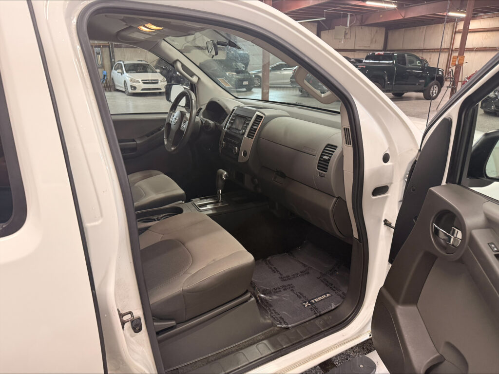 Front interior of a white pickup truck with the driver door open, showing steering wheel, center console, and cloth seats in view.
