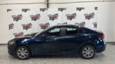 Side view of a dark blue sedan parked indoors in a showroom with a white wall and Wheel City Auto Finance Centers banners behind it.