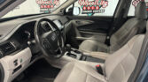 Interior of a gray-tan car showing steering wheel, dashboard, center console, and front/right seats with a dealership backdrop outside the windows