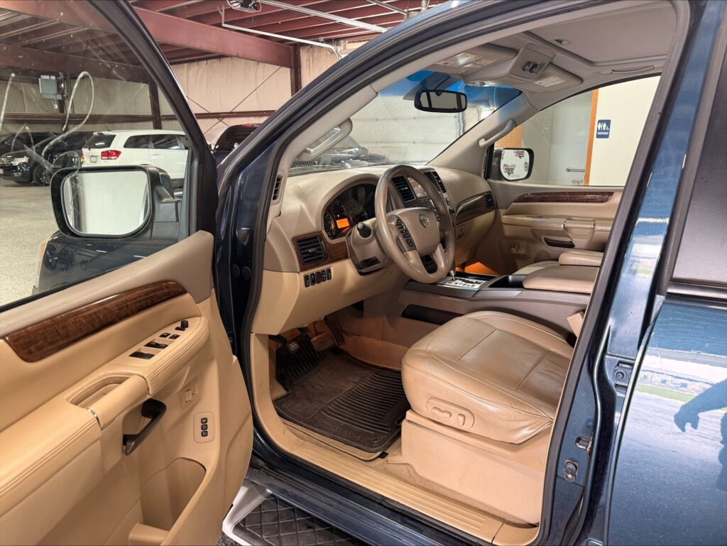 Driver's-side interior of a blue SUV with the door open, showing beige leather seats, wood trim, and center console setup in a garage.