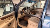 Driver's-side interior of a blue SUV with the door open, showing beige leather seats, wood trim, and center console setup in a garage.