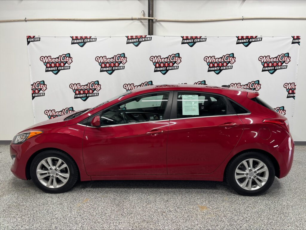 Red sedan indoors in front of a white backdrop covered with Wheel City Auto Finance Centers logos.