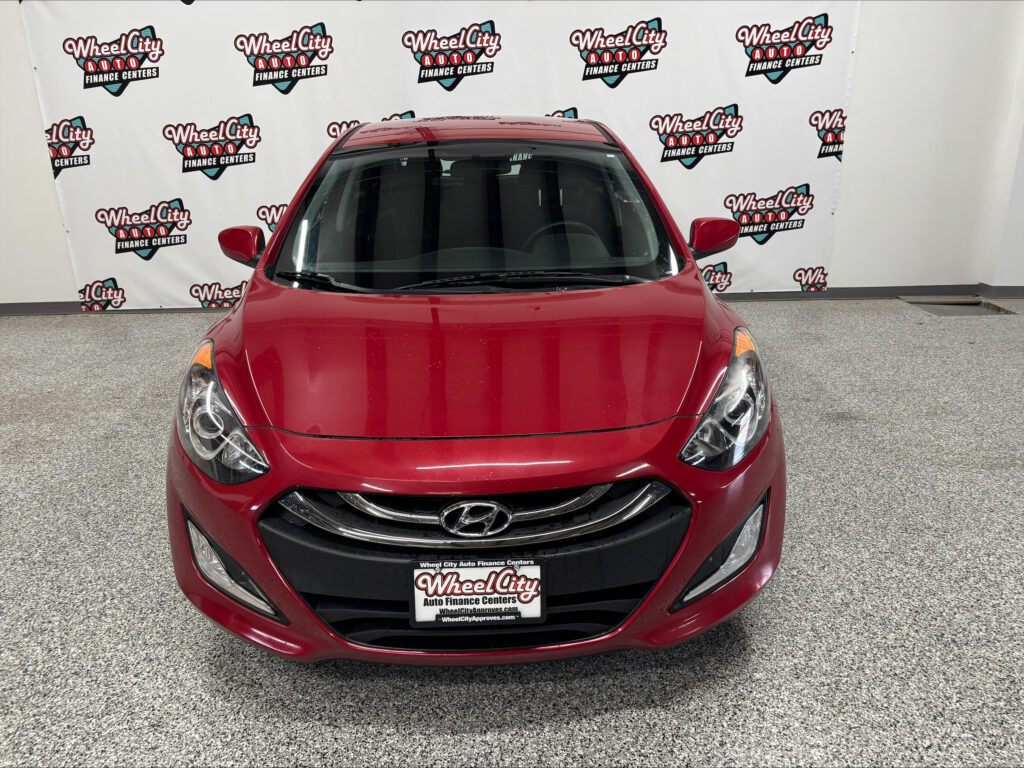 Front view of a red Hyundai car parked indoors with a Wheel City Auto Finance Centers backdrop behind it.