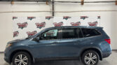 Blue SUV parked indoors in front of a Wheel City Auto Finance Centers banner on a white wall as ceiling pipes loom above it.
