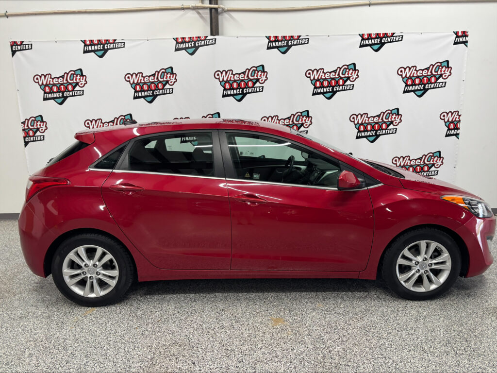 Red sedan parked indoors in front of a white backdrop with Wheel City Auto Finance Centers logos visible across the wall.
