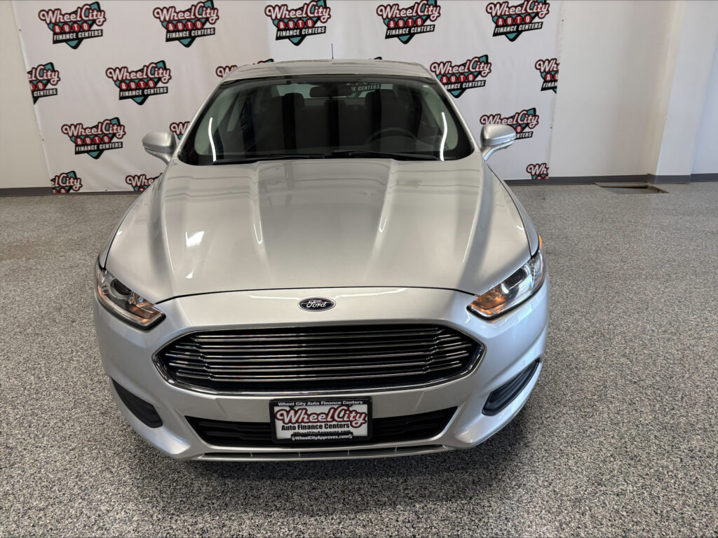 Front view of a silver Ford SUV in a showroom with Wheel City Auto Finance Centers backdrop logos behind it.