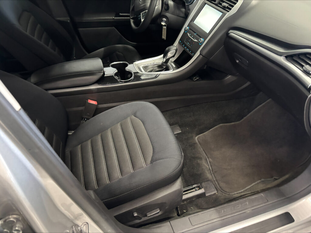 Front interior of a car showing the center console with gear shifter, cup holders, and black leather seats.