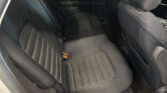 Back seat of a dark fabric car interior with vertical stitch lines and red seatbelt buckles visible at the bottom center.