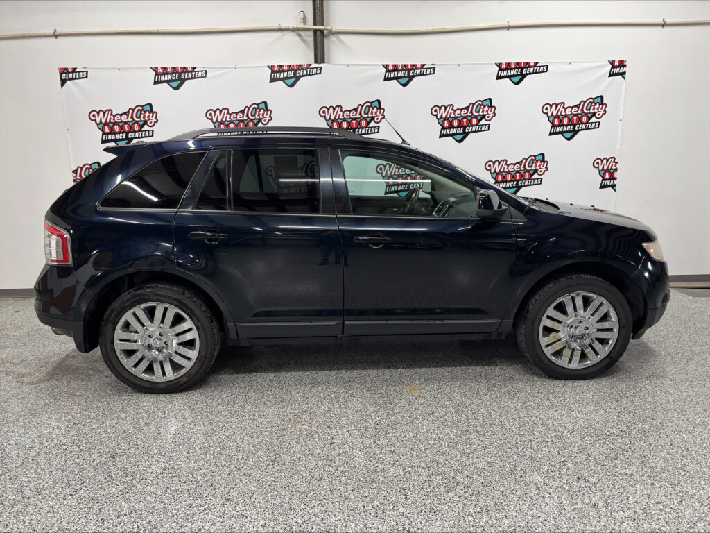 Side view of a dark blue SUV with chrome wheels parked indoors in front of a Wheel City Auto Finance Centers banner backdrop