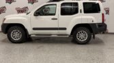 White Nissan Xterra SUV with roof rack and running boards, indoors in front of a Wheel City Auto backdrop.