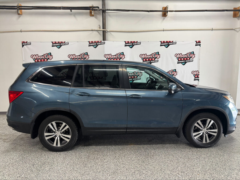 Side view of a blue SUV parked indoors in front of a Wheel City Auto banner with repeating logos on a white backdrop.