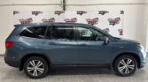 Side view of a blue SUV parked indoors in front of a Wheel City Auto banner with repeating logos on a white backdrop.