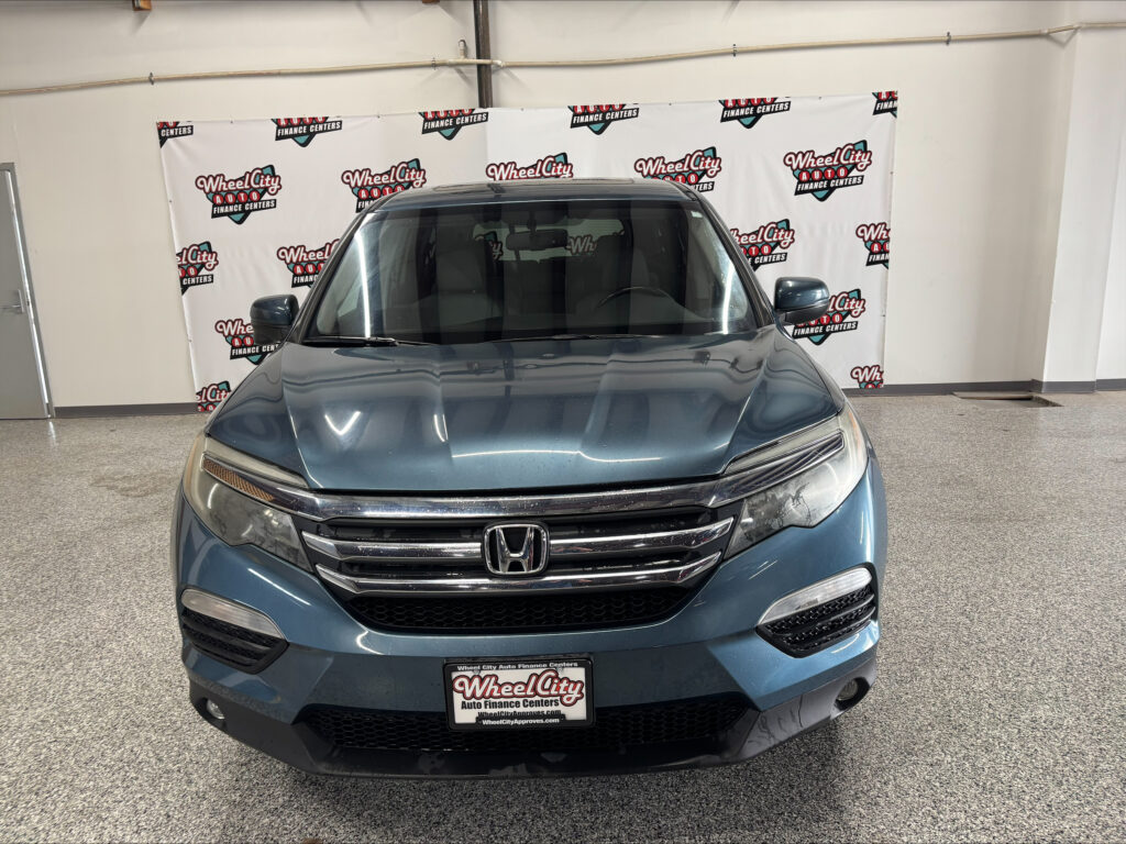 Front view of a blue Honda SUV indoors at a dealership, with a Wheel City Auto Finance Centers backdrop behind it.