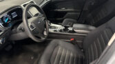 Interior of a car cockpit: steering wheel, center console with cup holders, and black front seats viewed from the passenger side.