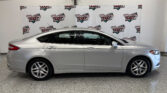 Side profile of a silver sedan parked indoors in front of a white backdrop with 'Wheel City Auto Finance Centers' logos repeated across the banner.