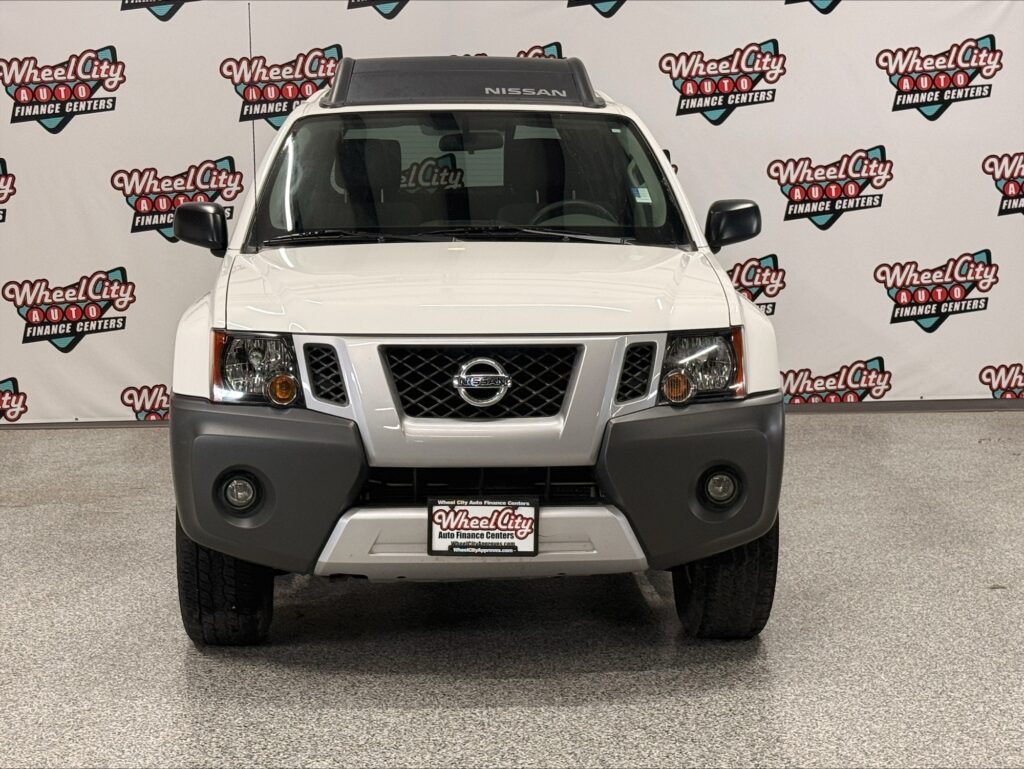 Front view of a white Nissan SUV in a showroom, featuring a gray bumper, Nissan emblem, and Wheel City backdrop behind it.