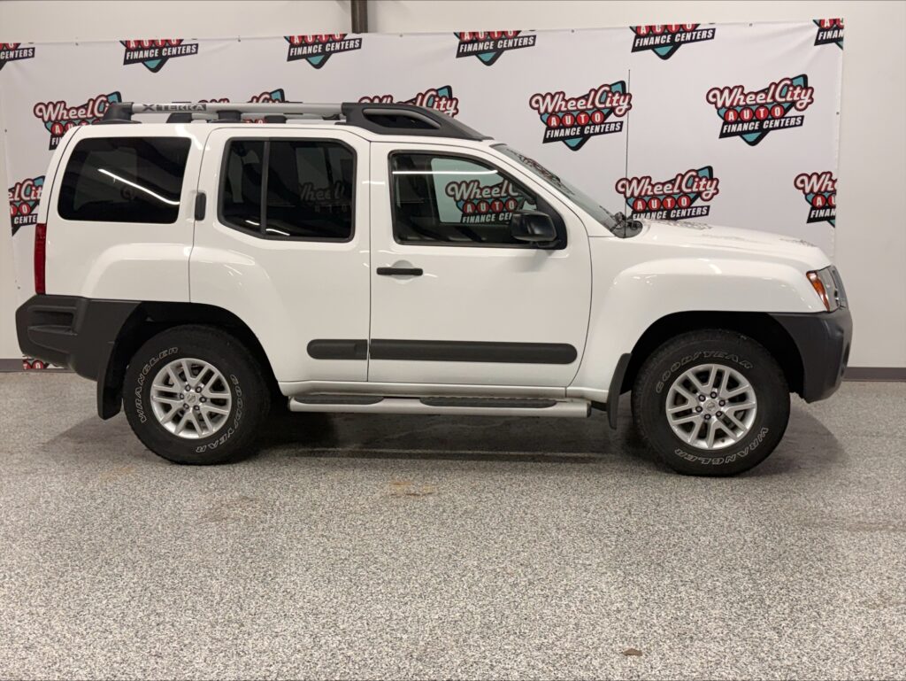 White Nissan Xterra/SUV shown in a dealership showroom, side profile with roof rack and running boards.