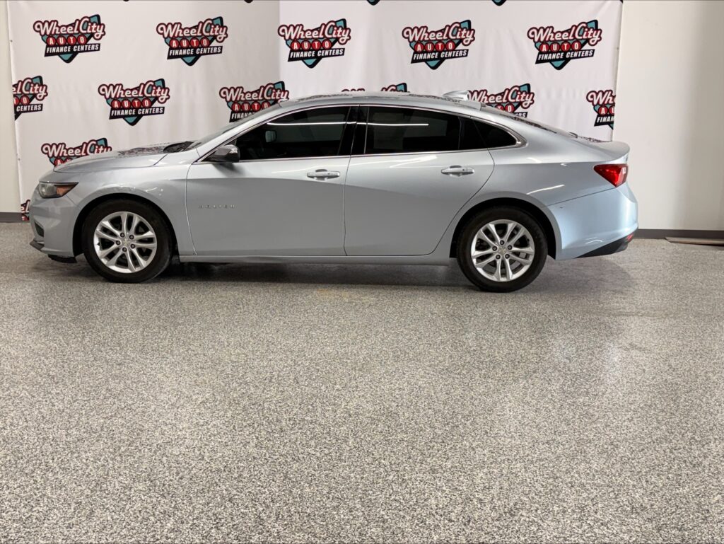 Side profile of a silver Chevrolet Impala sedan in a showroom with Wheel City Auto Finance Centers backdrop behind it.