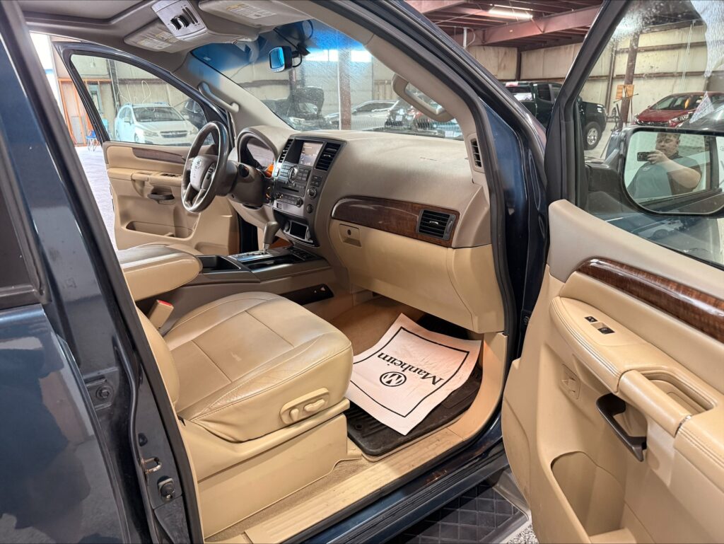Open driver’s door view of a blue SUV interior with beige leather seats, wood trim on the dashboard, and a center console visible.