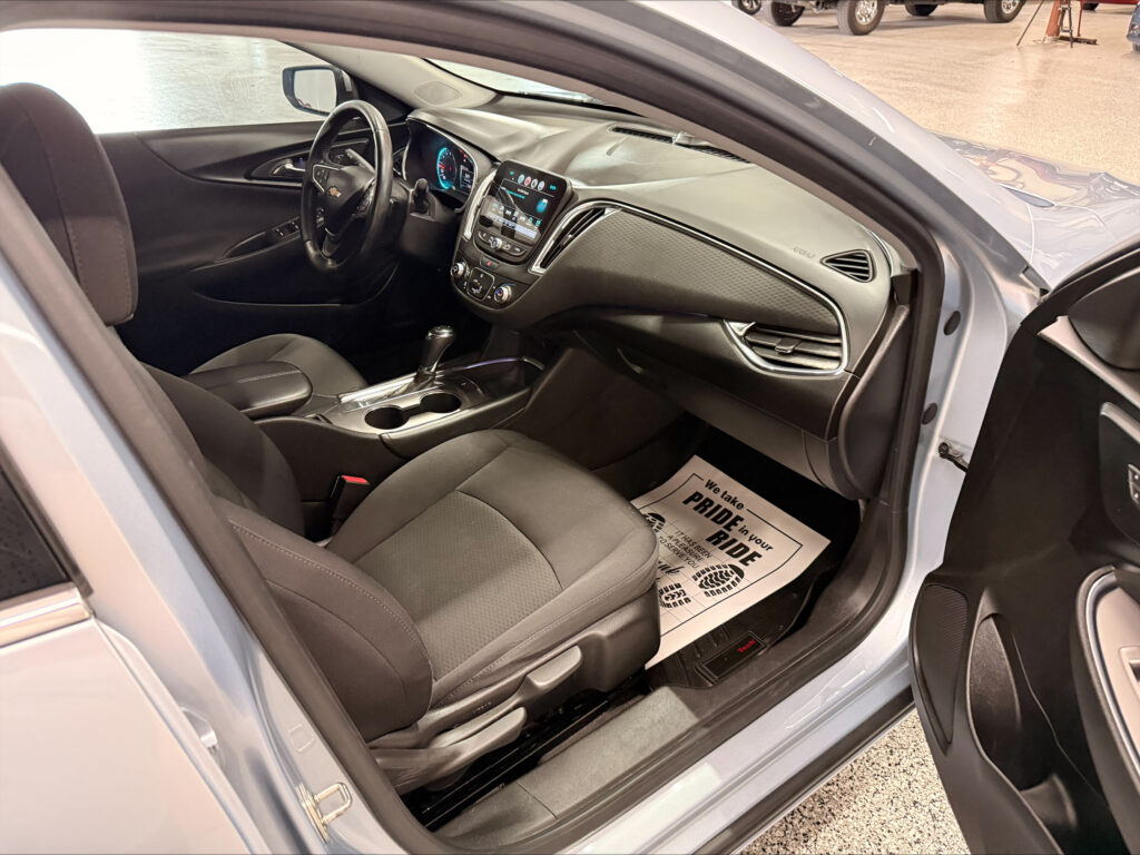 Interior of a modern car: driver and front passenger seats, dashboard with touchscreen center display, gear shifter, and cupholders visible from the open door.