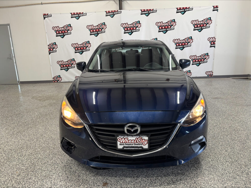 Front view of a dark blue Mazda parked indoors with a Wheel City Auto Finance Centers backdrop behind it