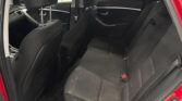 Rear passenger area of a red car with black fabric seats, headrests, and visible seat belts on a roomy back seat.