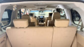 Interior of a beige SUV seen from the open rear hatch, third-row seats upright and cargo area visible, with headrest screens on the back of the front seats
